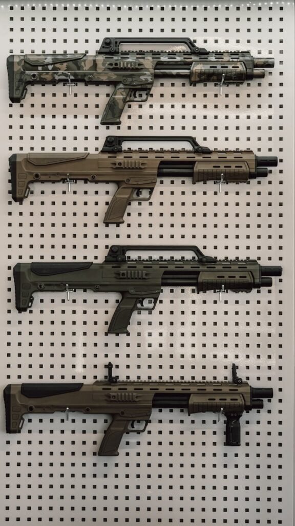 A collection of tactical rifles arranged vertically on a perforated wall for display.